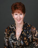 Smiling person in patterned blouse, dark background.