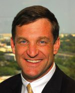 Smiling man in a suit with a cityscape background.