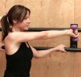 Woman exercising with a purple dumbbell against a wooden wall.