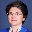 Professional portrait of a woman with short hair and glasses wearing a blue jacket.