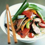 A bowl of Asian noodle soup with vegetables and chopsticks.