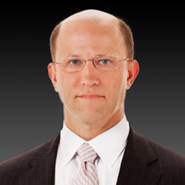 Professional man wearing glasses and a suit against a dark gradient background.