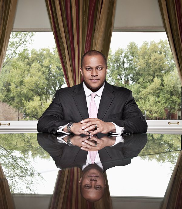 Confident businessman sits at a reflective table with hands clasped.