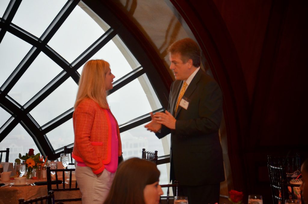 Two people engaged in conversation near a large window with a circular frame.