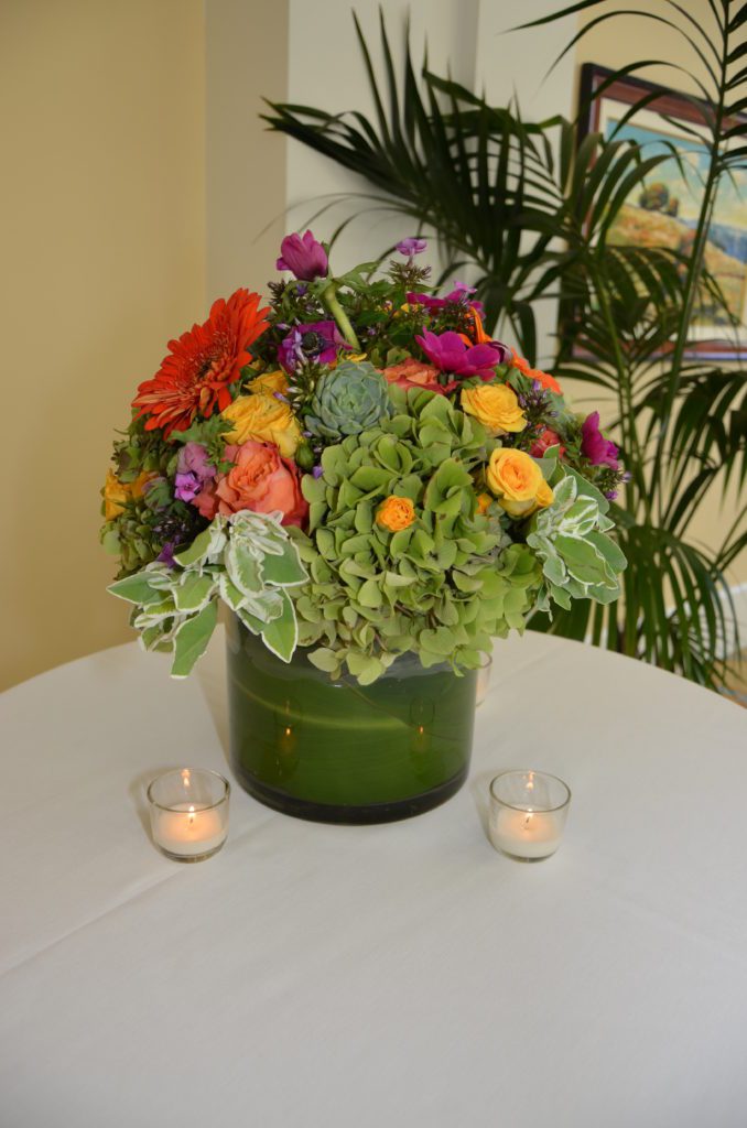 Colorful floral arrangement in a green vase with candlelight.
