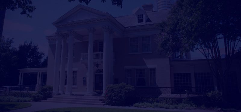Large historic building with columns and a porch at dusk.