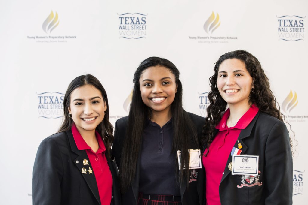 Three professional women smiling at a formal event with Texas-themed branding.