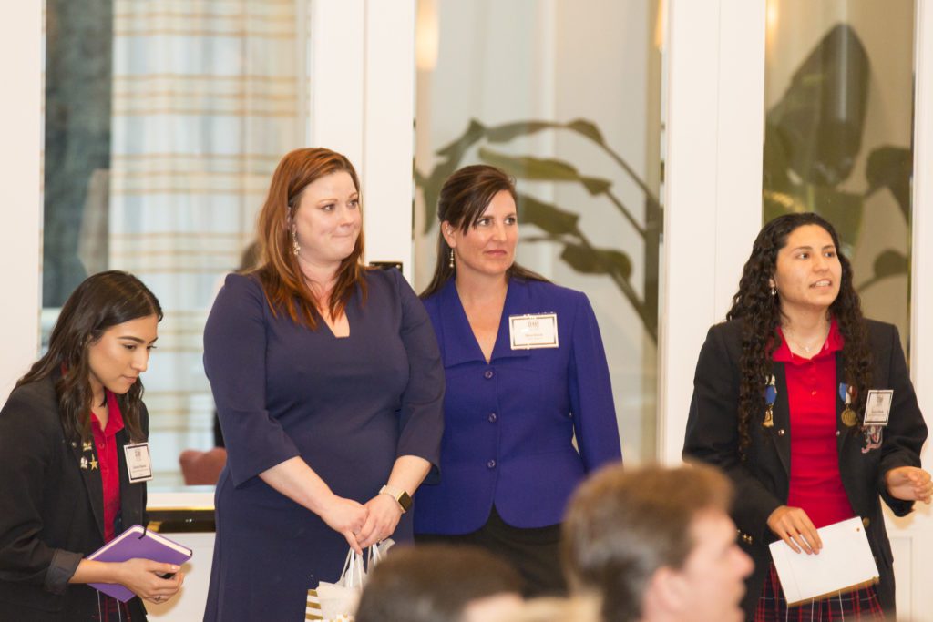 Two women standing and listening attentively at an indoor event.