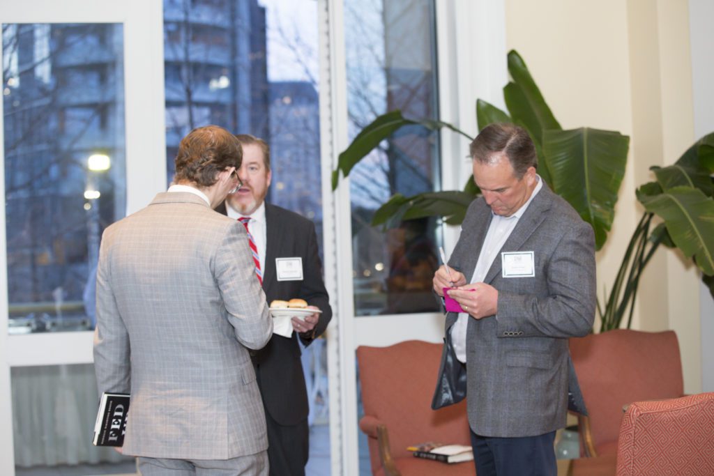 Three men in suits engaged in conversation at a formal event.