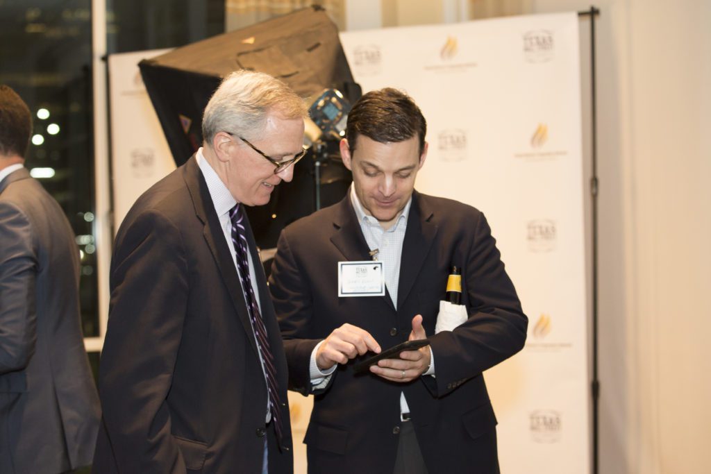 Two men in suits reviewing a phone at a formal event.