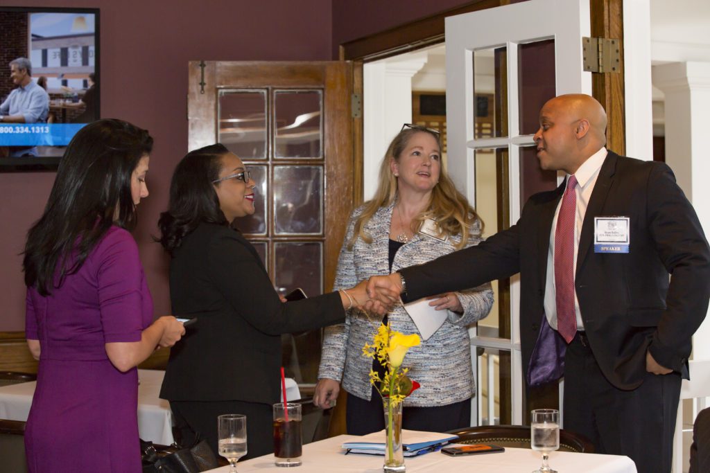 Two women shaking hands with a man during a meeting in a dining room.