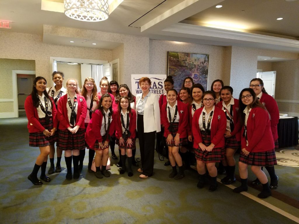 Group of students in uniforms posing with an older woman indoors.