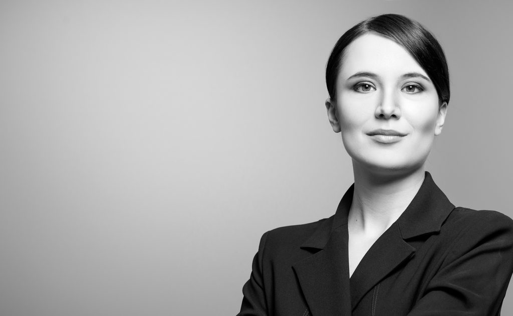 Confident woman in a black blazer posing against a gray background.