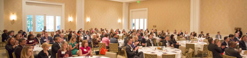 Audience attentively listens and applauds at a conference in a large meeting room.