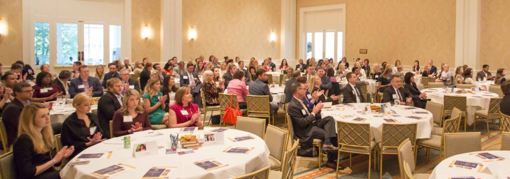 A large group of people attentively listening at a formal indoor event.
