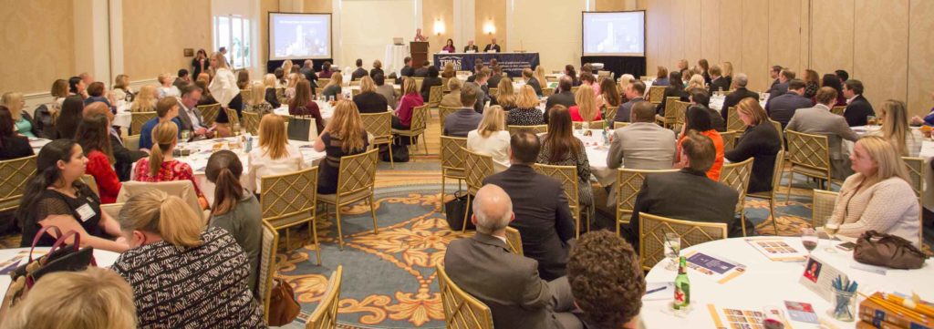 Audience attentively listening at a formal conference in a large banquet hall.