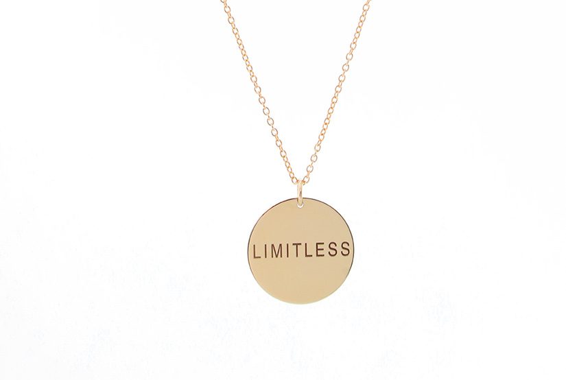 Gold necklace with a circular pendant engraved 'LIMITLESS'.