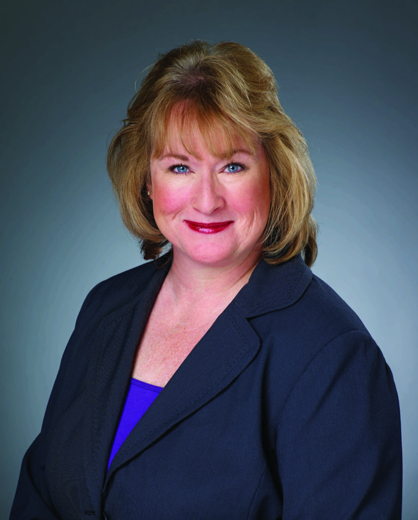 Professional portrait of a confident woman with blonde hair and a navy blazer.