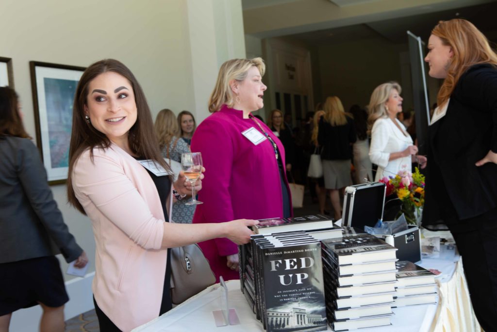 A woman smiles while holding a drink at a book signing event.