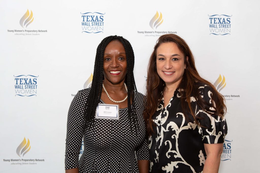 Two women smiling at a professional event with name tags, standing in front of a Texas-themed backdrop.