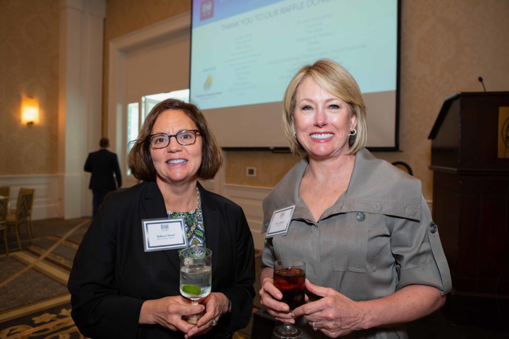 Two women at a social event holding drinks and smiling.