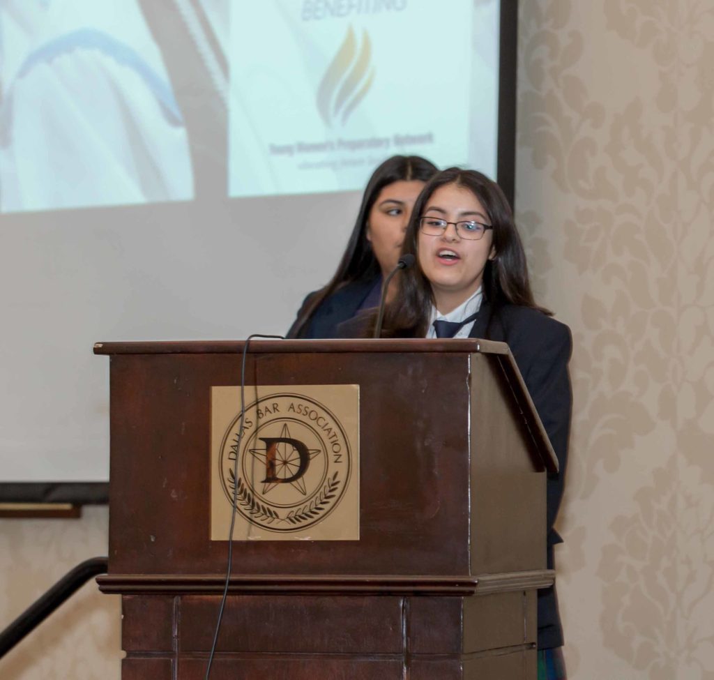 Young woman speaking at a podium in a formal setting.