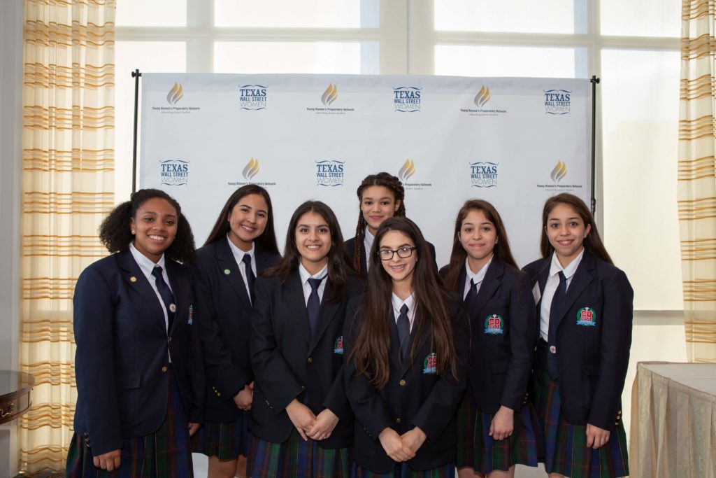 A group of smiling students in formal school uniforms posing indoors.