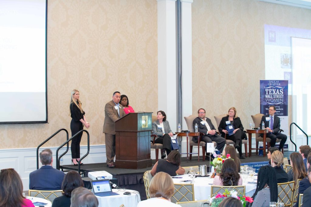 A woman speaks while others listen at a conference panel.