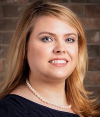 Professional woman smiling with pearl necklace and brick background.