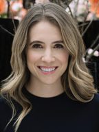 Smiling woman with wavy blonde hair wearing a black top.
