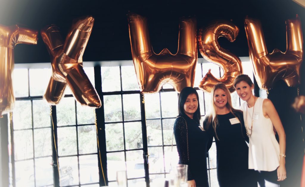 Three women posing by large gold balloon letters spelling 'KWS'.