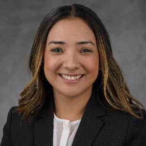 Professional woman smiling in business attire against a gray background.