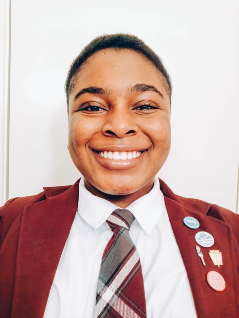Smiling person in formal attire with pins on lapel.