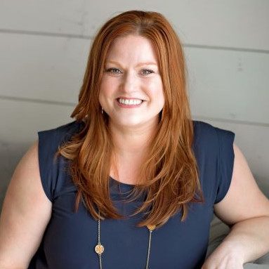 Smiling woman with long red hair in a navy blue top.