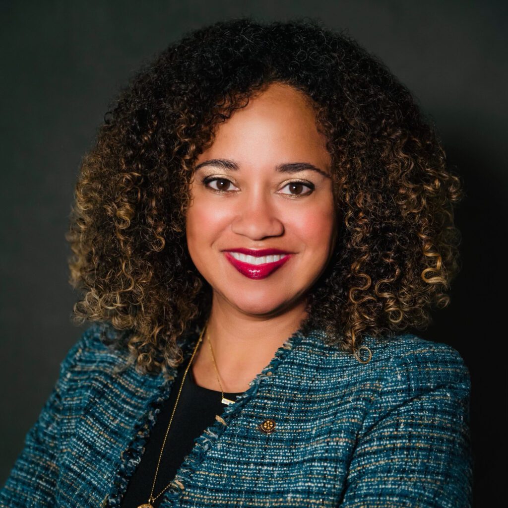 Professional woman with curly hair in a blue checkered blazer smiling.