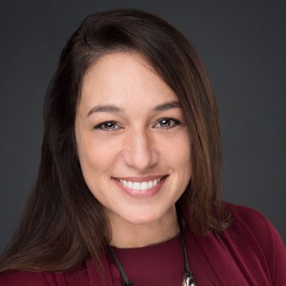 Smiling young woman with long brown hair against a dark background.