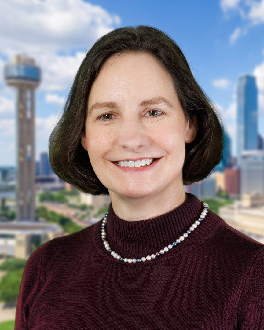 Smiling woman in maroon sweater and pearl necklace with cityscape background.