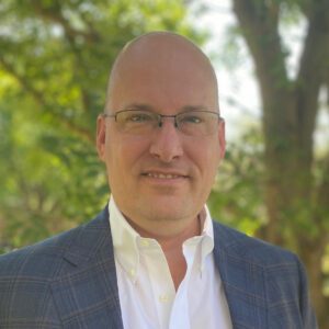 Man with glasses and suit outdoors.