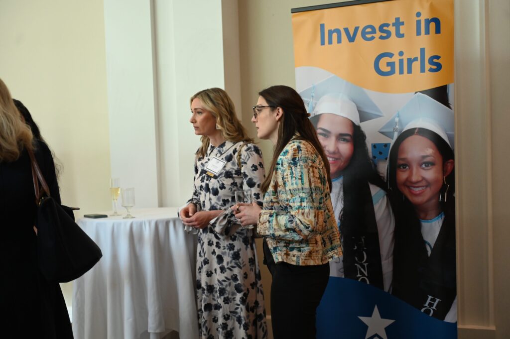 Women standing near "Invest in Girls" banner.